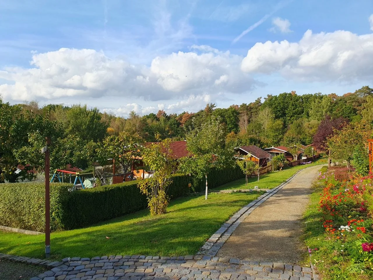 Kiesweg zwischen Beeten, links hinter der Hecke der Spielplatz, dahinter die Hütten
